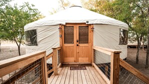 En yurt med træterrasse, en midterplaceret dør og en overdækket indgang.