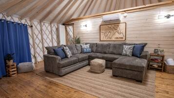 A cozy interior with a sectional sofa, ottoman, and a wall-mounted air conditioner.