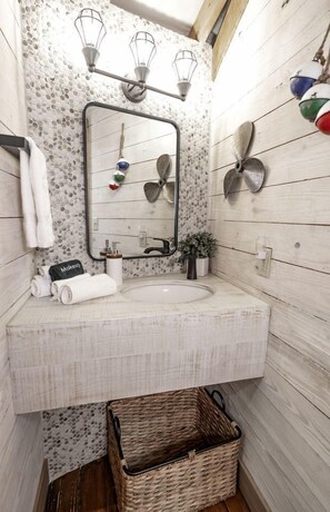 Une salle de bain avec un mur en bois, un miroir, un lavabo et un luminaire suspendu.