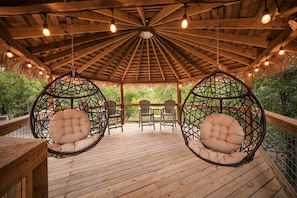 Terraza de madera con sillas colgantes y una estructura de techo de paja.