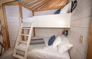 Une chambre avec un lit superposé, une échelle, des oreillers et une couverture.