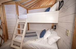 Une chambre avec un lit superposé, une échelle, des oreillers et une couverture.