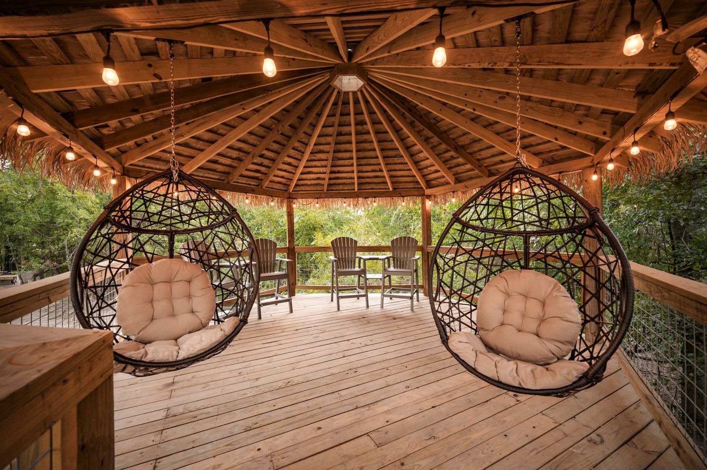 A wooden deck with hanging chairs and a thatched roof structure.