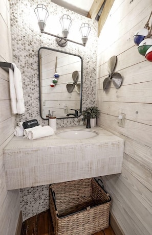 Un baño con pared de madera, un espejo, un lavamanos y una lámpara colgante.