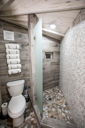 Un bagno con soffitto in legno, un water, una doccia con parete strutturata e un appendi asciugamani.