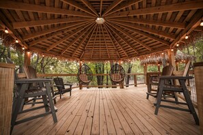 Une terrasse en bois avec des chaises suspendues et une structure de toit en chaume.