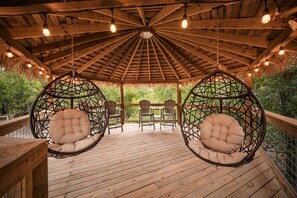 Une terrasse en bois avec des chaises suspendues et une structure dotée d’un toit de chaume.