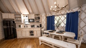 A rustic kitchen with wooden cabinets, a black refrigerator, and a dining table with benches. - Family-Friendly Yurt with Hot-Tub near to the Medina River in Bandera, Texas (Bandera)