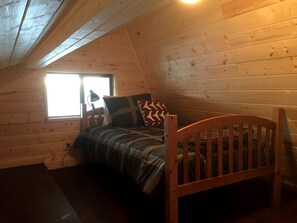 A small, cozy room with a single bed, a window, and wooden walls.