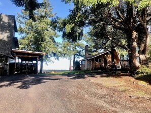 Une cabane rustique dotée d’un porche abrité, d’une cheminée en pierre et d’un grand arbre au premier plan.