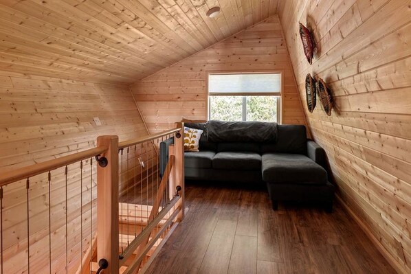A wooden interior with a wooden staircase, a black sofa, and a window with blinds.