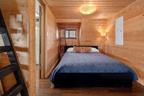 Quarto de cabana de madeira com beliche, escada, mesa de cabeceira e janela com persianas.
