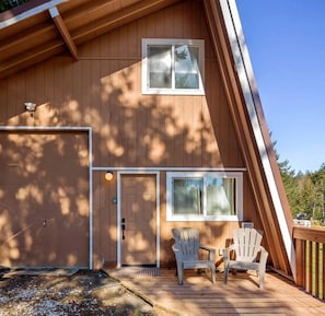 Una cabaña de madera con garaje, dos ventanas y un porche con dos sillas Adirondack.