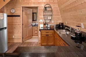 A compact kitchen with wooden cabinetry, a stainless steel refrigerator, a coffee maker, and a kettle.
