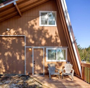 Uma cabana de madeira com garagem, duas janelas e um alpendre com duas cadeiras Adirondack.