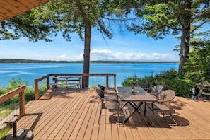Una terraza de madera con una mesa y sillas, con vista a un lago.