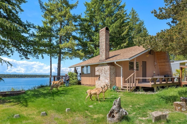 Eine Holzhütte mit einem Steinkamin, einer Holzterrasse und Blick auf einen See.