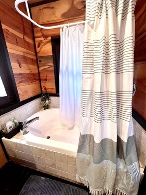 Ein Badezimmer in einer Holzhütte mit einer Badewanne, einer Duschvorhang und einem Handtuchhalter.