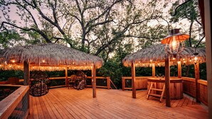 Una terrassa de fusta amb gazebos de palla, cadires de fusta i un bany d'hidromassatge.