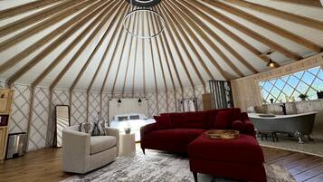 A yurt interior with a round skylight, a sofa, a red couch, a bathtub, and a kitchen area.