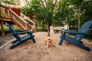 Une terrasse en bois avec deux fauteuils Adirondack, une bouteille de vin et un barbecue.