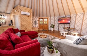 Un ambiente accogliente con un divano rosso, una poltrona grigia, pareti in legno, una TV e un tavolo di legno.