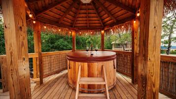 A wooden gazebo with a hot tub, wooden deck, and a view of greenery.