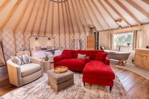 A yurt interior with a bed, red sofa, wooden floor, and a bathtub. - Love Bird Yurt Romantic, Hot Tub, by the River in Bandera, Texas (Bandera)