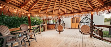 Una terraza de madera con sillas colgantes y una estructura de techo de paja.