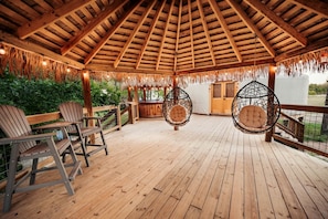 A wooden deck with hanging chairs and a thatched roof structure. - Love Bird Yurt Romantic, Hot Tub, by the River in Bandera, Texas (Bandera)