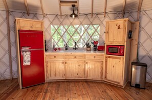 A compact kitchen with wooden cabinets, a red refrigerator, a sink, and a microwave. - Love Bird Yurt Romantic, Hot Tub, by the River in Bandera, Texas (Bandera)