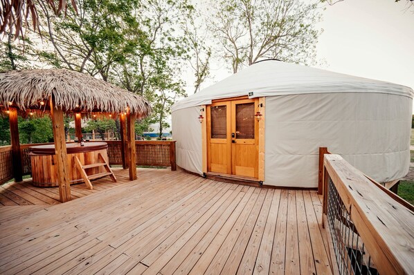 A wooden deck with a thatched gazebo, a wooden bar, and a large white tent with a wooden door.