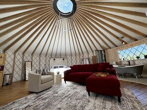 A yurt interior with a round skylight, a sofa, a red couch, a bathtub, and a kitchen area. - Love Bird Yurt Romantic, Hot Tub, by the River in Bandera, Texas (Bandera)