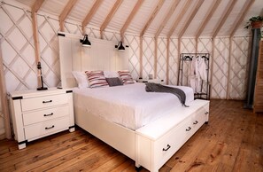 A bedroom with a white bed, wooden floor, and a white wardrobe with drawers.
