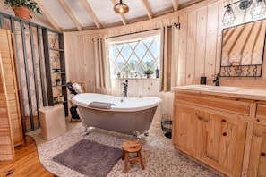A bathroom with a freestanding bathtub, wooden cabinets, a window with a view, and a mirror with a sun design.