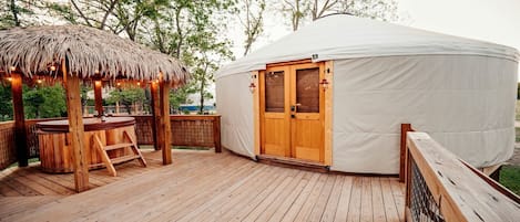 Una terraza de madera con un pabellón de paja, una barra de madera y una gran carpa blanca con una puerta de madera.