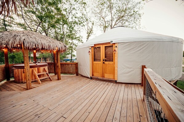 A wooden deck with a thatched gazebo, a wooden bar, and a large white tent with a wooden door.