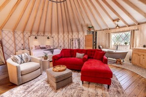 A yurt interior with a bed, red sofa, wooden floor, and a bathtub. - Love Bird Yurt Romantic, Hot Tub, by the River in Bandera, Texas (Bandera)