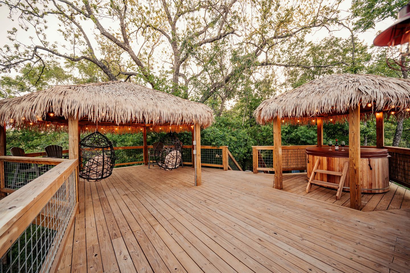 A wooden deck with thatched umbrellas, chairs, and a hot tub.