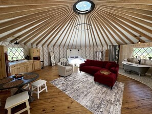 A yurt interior with a dining area, sofa, and a bathtub. - Love Bird Yurt Romantic, Hot Tub, by the River in Bandera, Texas (Bandera)