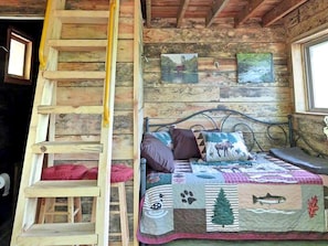 Een rustiek houten interieur met een trap, een bed met sprei en twee ingelijste foto’s aan de muur.