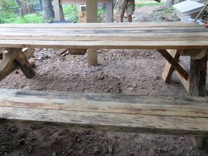 A rustic wooden picnic table with a simple, sturdy design, set in a natural, outdoor environment.