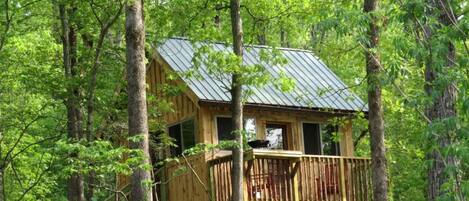 A wooden cabin with a balcony, surrounded by trees.