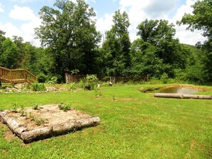 A grassy outdoor area with a wooden deck, a small pond, and trees in the background.