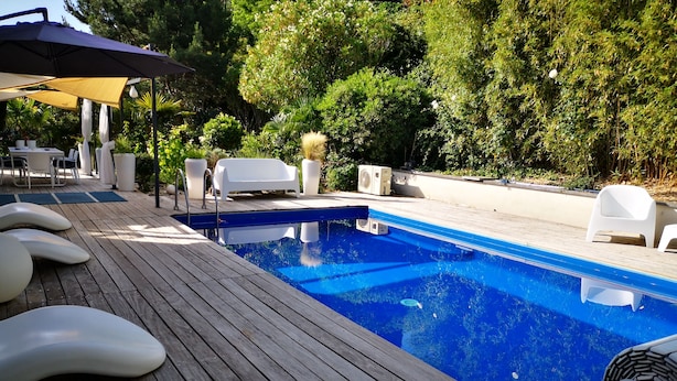 Una piscina con bordo in legno, poltrone da relax bianche e un'area salotto coperta.