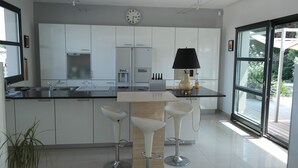 Una cucina moderna con mobili bianchi, un'isola centrale con sgabelli, una sveglia e un'ampia finestra.