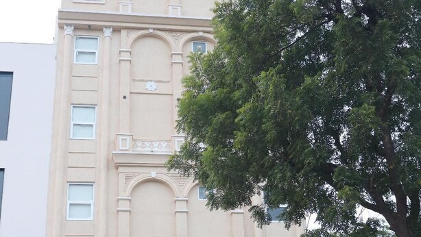 Um hotel com fachada bege, entrada central com porta de vidro e um letreiro que diz 'HOTEL AARAMBH'.