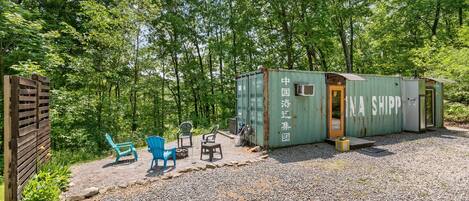 A rustic cabin with a gravel driveway, surrounded by trees.