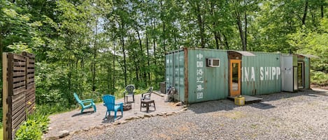 A rustic cabin with a gravel driveway, surrounded by trees.