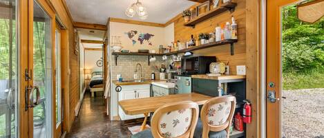 Interior acogedor de una cabaña con una mesa de comedor de madera, dos sillas, una zona de cocina con microondas y un mapa mundial en la pared.